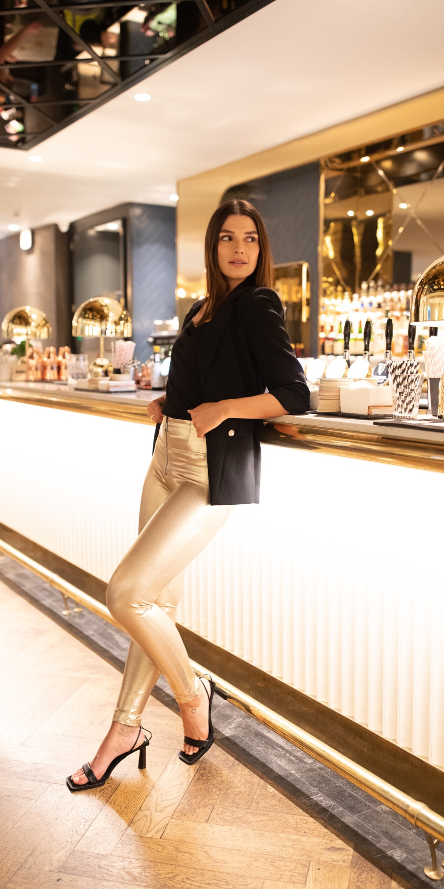 Freddy WR.UP® gold metallic trousers styled with a black blazer at a bar